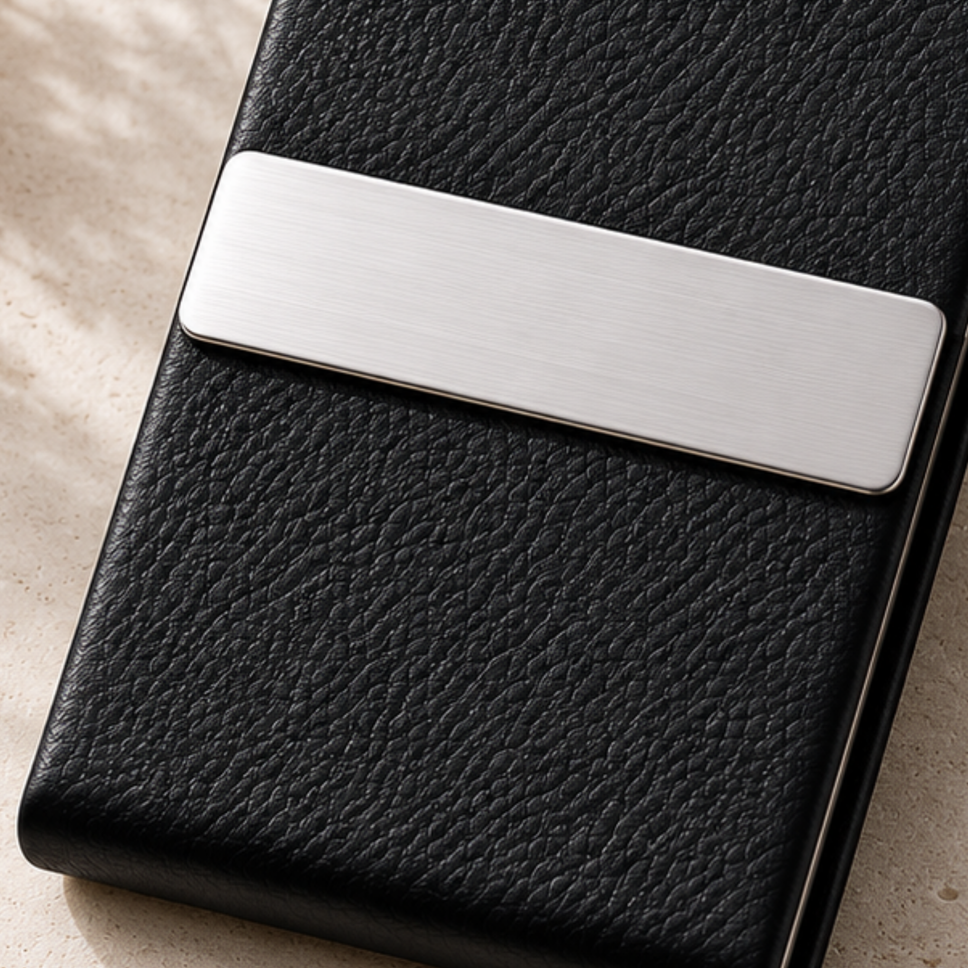 Black leather wallet with a silver metal clasp on a beige surface