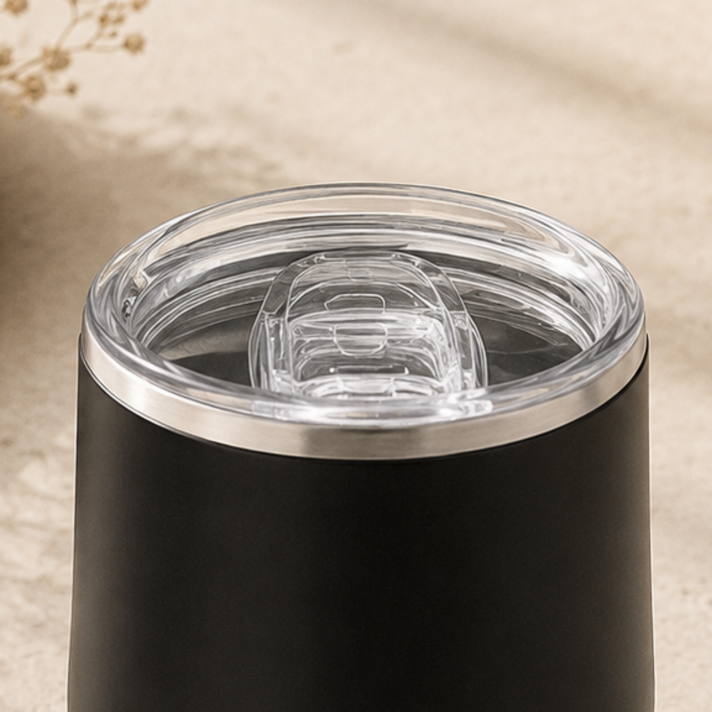 Close-up of a black tumbler with a clear lid on a beige background