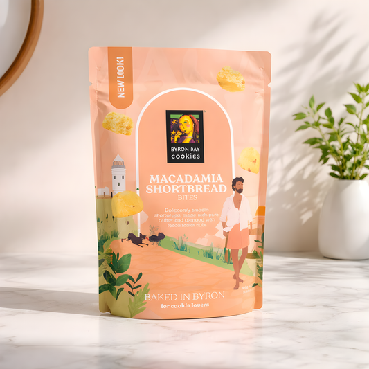 Packaging of Byron Bay Cookies Macadamia Shortbread Bites on a light surface with a plant in the background.