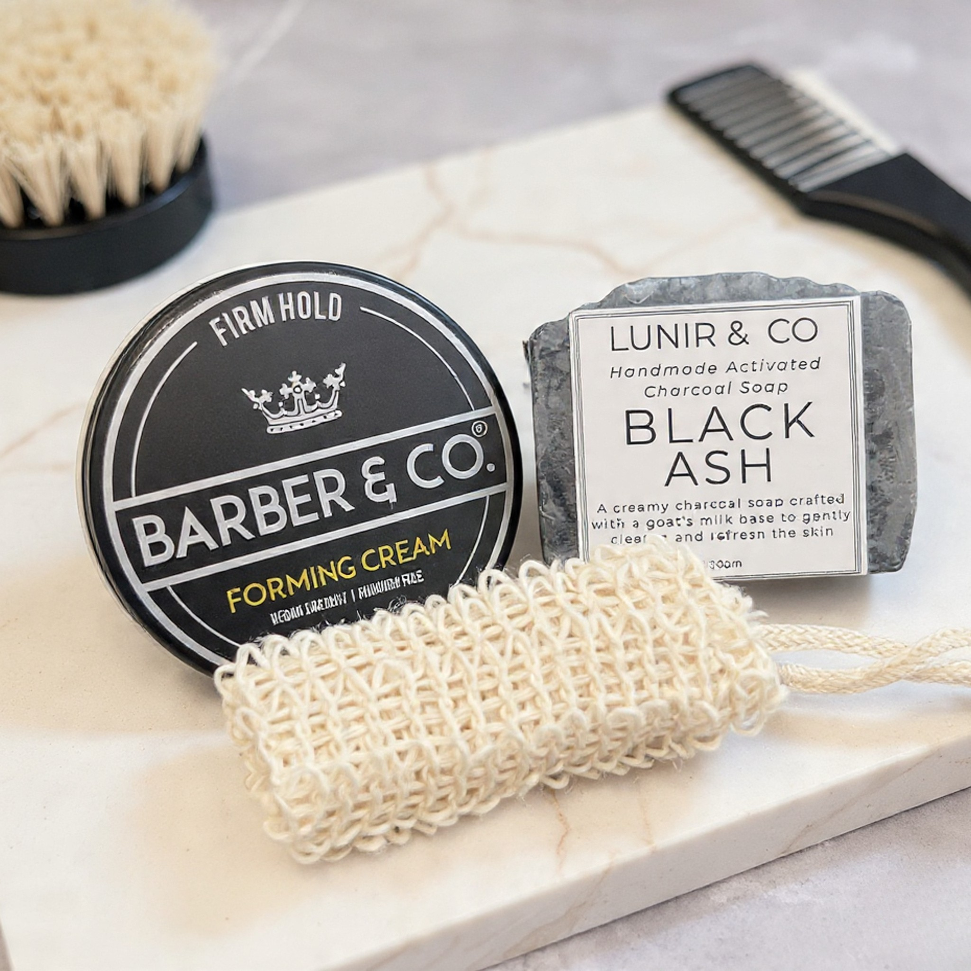 Barber & Co. forming cream, Lunir & Co. black ash soap, and a loofah on a marble surface.