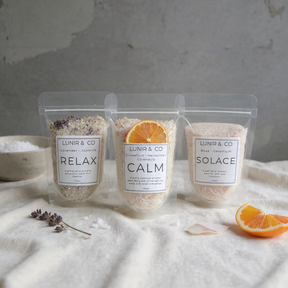 Three packages of LUNIR & CO bath salts on a textured surface with oranges and lavender.