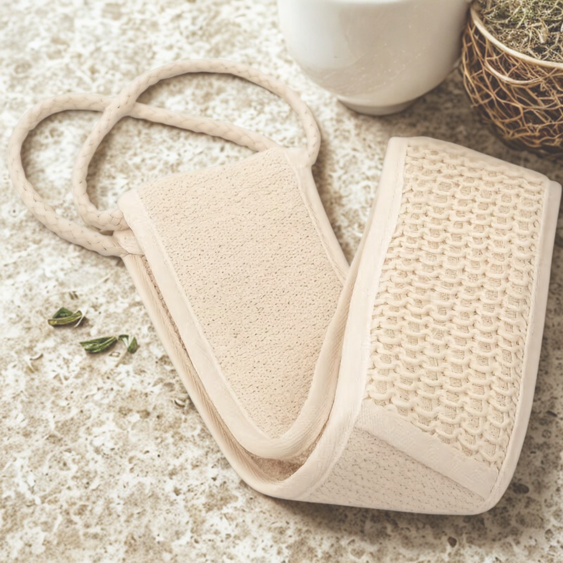 Beige bath mitt and scrubber on a textured surface with a cup in the background