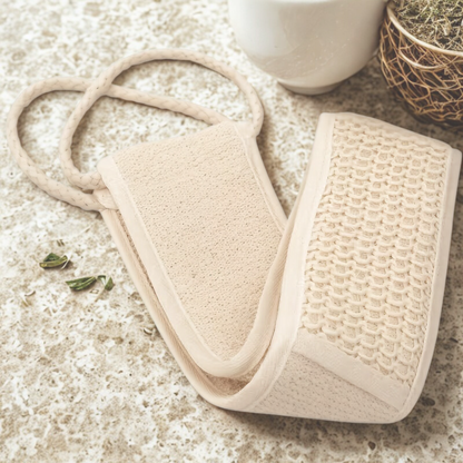 Beige bath mitt and scrubber on a textured surface with a cup in the background
