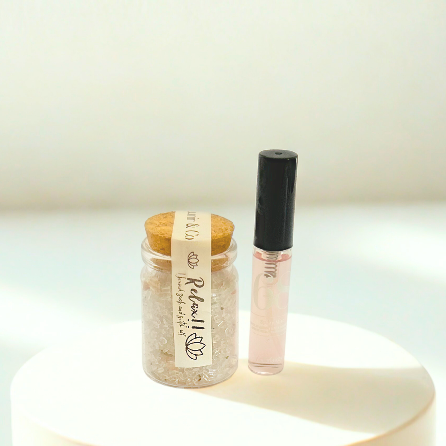 Small jar with cork lid and a clear bottle with black cap on a light background