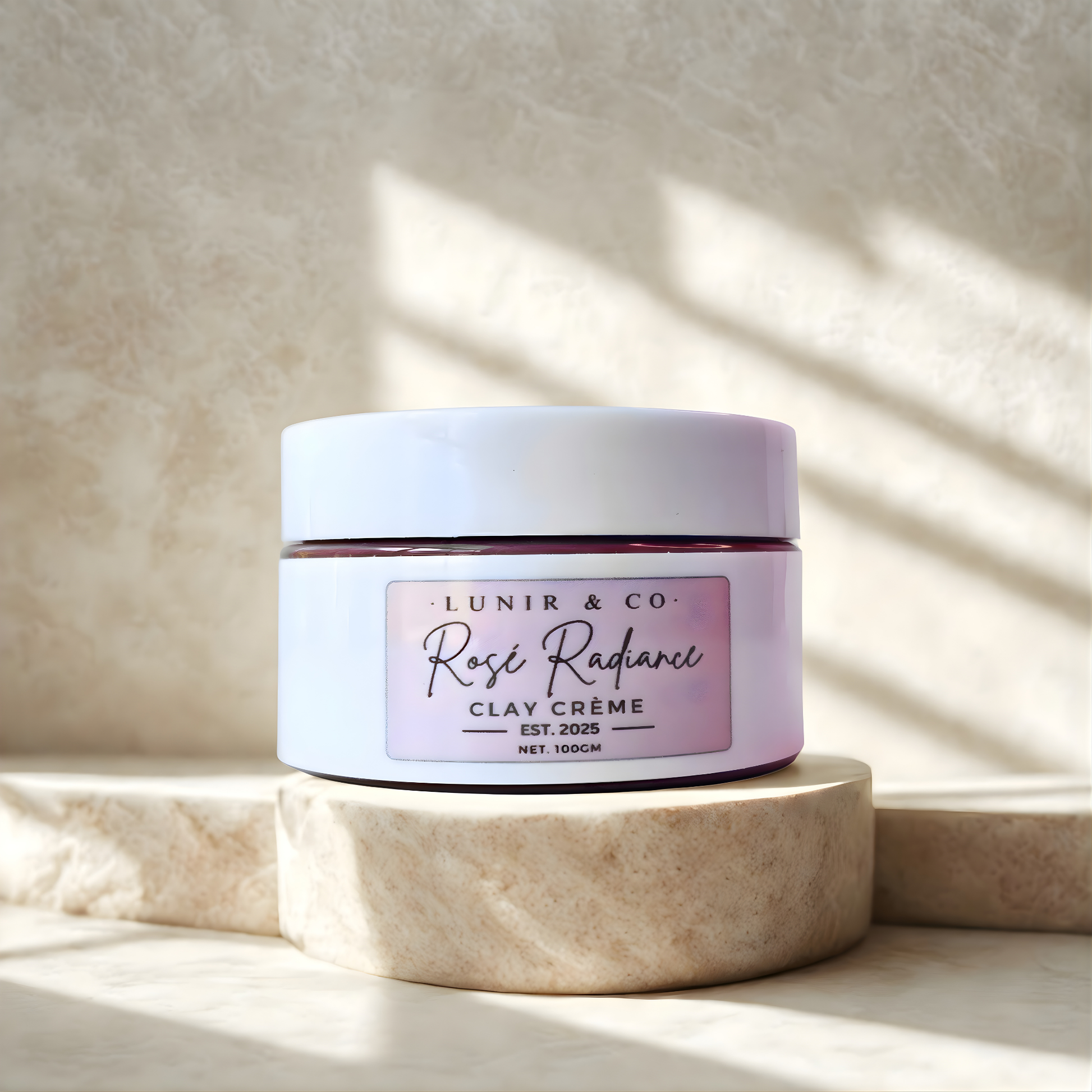 Jar of 'Rosie Radiance Clay Crème' by Lunir & Co. on a beige stone surface with soft shadows.